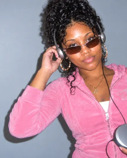 A woman with tinted glasses, headphones, and a pink tracksuit holds a portable CD player.